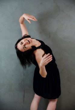 Model Standing right in front of the camera with vivid emotions. Vertical portrait of a cute smiling brunette woman in black dress on gray alternative background.