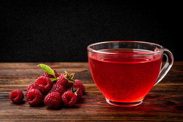 Cup of  tea with raspberry on dark wooden background.
