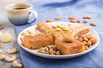 traditional arabic sweets (basbus, kunafa, baklava), a cup of coffee and nuts on a gray concrete background  side view, selective focus.