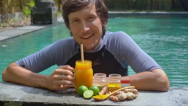 A young man drinks the national Balinese drink Jamu swimming in the swimming pool