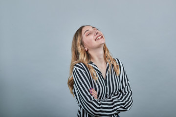 Happy young blonde woman in fashion black and white striped shirt keeping hands crossed, smiling...