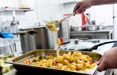Chef cooks fried potatoes with pieces of meat in a restaurant kitchen
