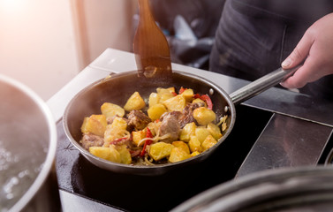 Chef cooks fried potatoes with pieces of meat in a restaurant kitchen