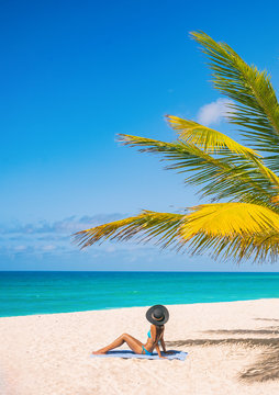 Caribbean beach tourist relaxing in Barbados, cruise shore day. Woman sunbathing sun tanning under palm tree on sand on Dover beach, famous resort tourist tropical destination.