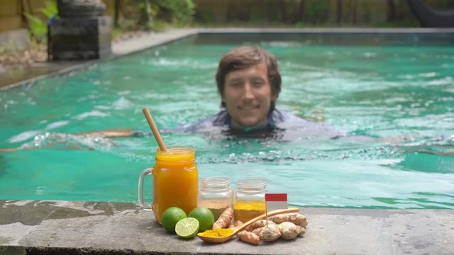 A young man drinks the national Balinese drink Jamu swimming in the swimming pool