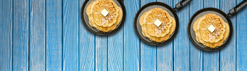 Frying pans with hot delicious pancakes on blue wooden background. Pancake week. Panoramic banner.