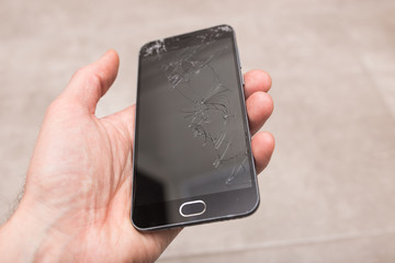 Hand holds a broken smartphone. Phone screen in cracks.