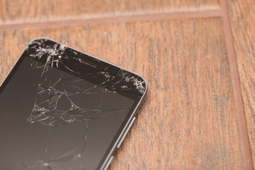 A broken phone is on the floor. Smartphone cracked screen closeup.