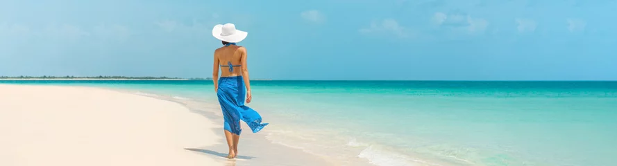 Fototapeten Luxury beach vacation elegant tourist woman walking relaxing in beachwear hat on white sand Caribbean beach. Lady tourist on holiday vacation resort. Banner panorama landscape. © Maridav