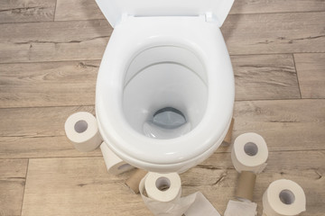 white toilet on a wooden floor in retro style. there are many rolls of toilet paper around it.