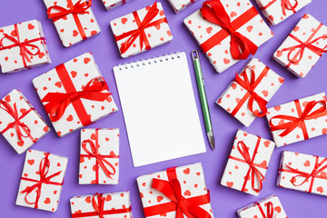 Fototapeta na wymiar Holiday composition of notebook and gift boxes with red hearts on colorful background with empty space for your design. Top view of Valentine's Day concept