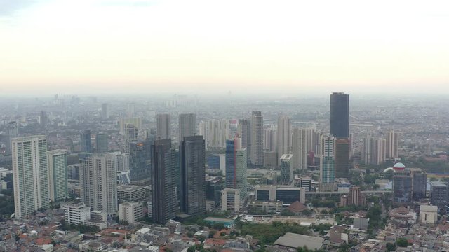 Aerial view of skyscrapers in Jakarta with building in construction before beautiful sunset and cloudy sky.  Fast Dolly motion