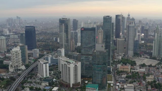 Aerial view of skyscrapers in Jakarta with building in construction before beautiful sunset and cloudy sky.  Fast Dolly motion
