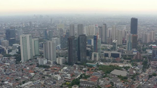 Aerial view of skyscrapers in Jakarta with building in construction before beautiful sunset and cloudy sky.  Fast Dolly motion