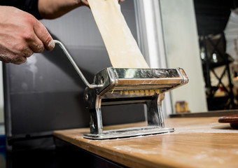 Chef rolling dough with a pasta machine. Pasta maker machine. Homemade italian style cuisine. Restaurant.