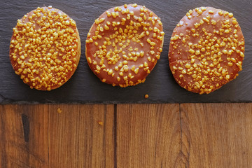 Three chocolate doughnut with golden crumb on a stone plate.
