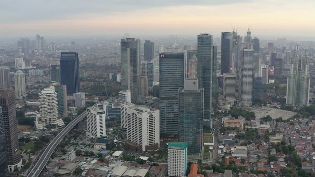 Aerial view of skyscrapers in Jakarta with building in construction before beautiful sunset and cloudy sky.  Fast Dolly motion