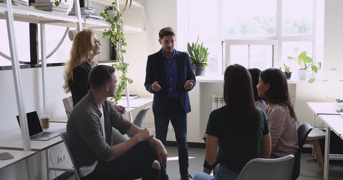Confident male leader speaking to diverse friendly team in office