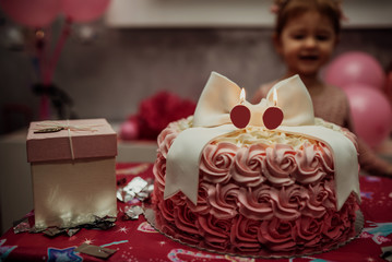 2 year baby girl in pink dress with her first birthday cake, happy birthday card,a cute little girl celebrates her first birthday surrounded by gifts