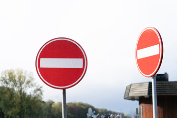 Two red circular traffic signs or roadsign with a white bar indicating no entry on a grey metal post against a cloudy sky in a forest area