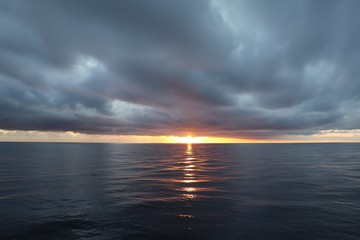 Fototapeta na wymiar Narrow strip of sunset over the calm sea and very dark dense clouds