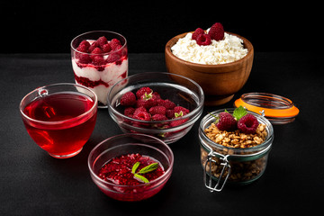 Raspberry and food with this berry on black background. Raspberry jam, tea, granola, cottage cheese and yogurt.