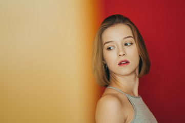 Closeup portrait of a model girl on a red background, looks all the way to the yellow part of the photo. Cute girl looks at the yellow glare with a serious face. Copy space