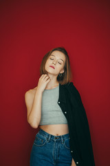 Portrait of sexy girl in t-shirt and shirt on red background, posing at camera with closed eyes. Attractive model poses on camera, closed her eyes with pleasure. Vertical photo.