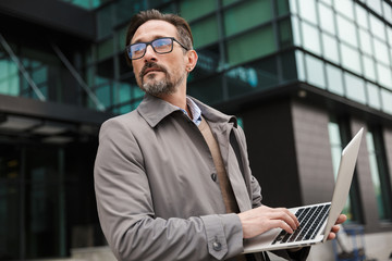 Image of mature bearded businessman using laptop while standing