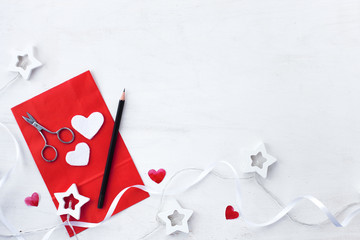 Valentines day composition with  heart, garland, red greeting card and pencil on a rustic white background. February 14 greeting card. flat lay with copy space vertical