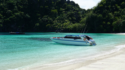 White color speed boat parking on the water with beautiful beach background