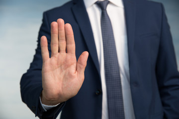 Businessman gesture. Male palm close-up in a gesture of stop. In the background a man in a suit with a tie. - obrazy, fototapety, plakaty
