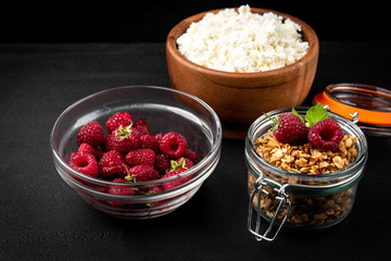 Cottage cheese, granola and fresh raspberry on black background.