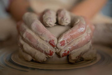 Close-up view of woman hands working on pottery wheel and making clay pot. Hands sculpts a cup from...