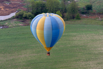 Obraz premium Hot-air balloon drifting toward the ground, field and trees on the background