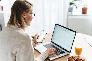Photo of happy caucasian woman typing on laptop and cellphone