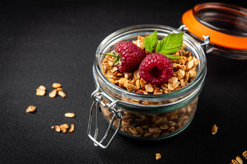 Granola in glass jar and raspberry on black background.
