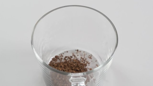 Spoon with instant coffee puor in a white mug on a black background. Slow motion.