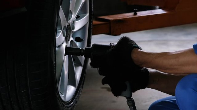 Car mechanic using air wrench torque for remove wheel nuts.