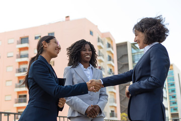 Happy positive partners meeting and talking near office building. Business women shaking hands with each other outside in city. Partnership and handshake concept