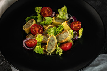 traditional German maultaschen, baked with purple onion, fresh tomatoes and young salad on a dark background