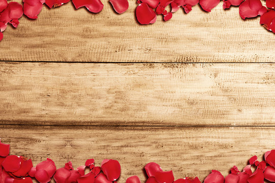 The frame of red rose petals with a wooden table background