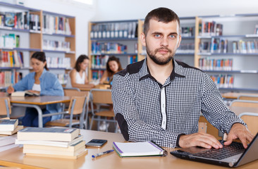 Fototapeta premium Young male student working with laptop and books in university library