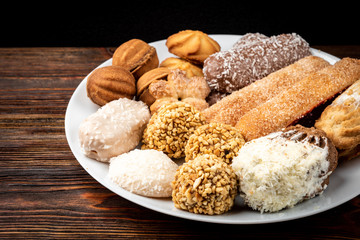 Different types of cookies on white plate on dark wooden background.