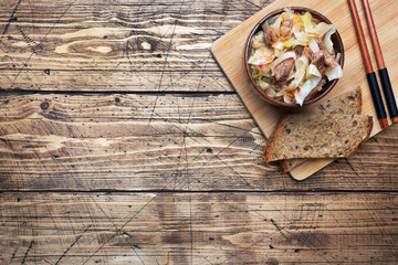 Stewed cabbage with meat in a wooden bowl on a wooden background. Traditional Russian dish of Solyanka. Copy space