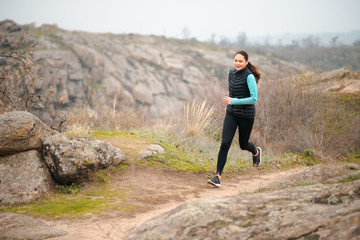 Fototapeta premium Beautiful Smiling Woman Running on the Mountain Trail at Cold Autumn Evening. Sport and Active Lifestyle.
