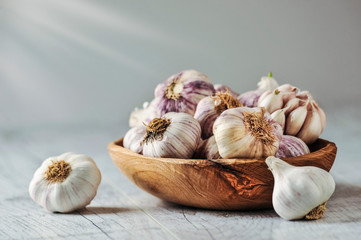 Garlic Cloves and Bulb in wooden bowl on white table.