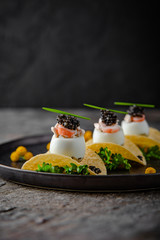 Luxurious appetizer of quail eggs with a paste of squid, shrimp and black caviar on potato and cheese chips. - obrazy, fototapety, plakaty