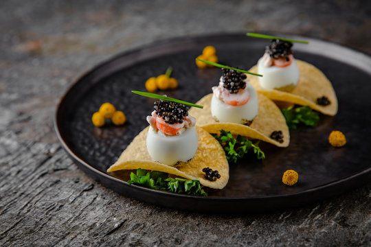 Luxurious appetizer of quail eggs with a paste of squid, shrimp and black caviar on potato and cheese chips.