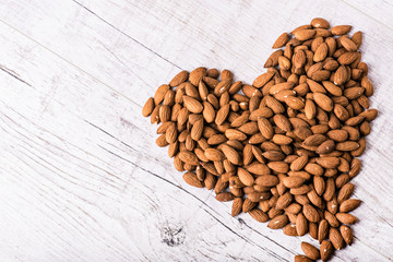 Almonds nut on white wooden table. Almond healthy raw food in heart shape.